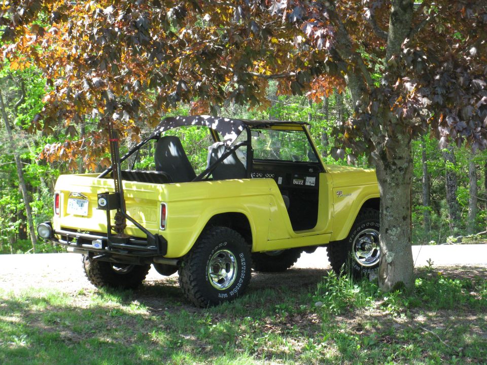 Yellow 1973 Ford Bronco with doors removed, parked under a tree