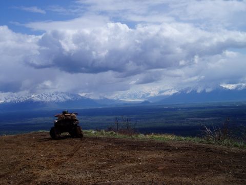 2000 Ford E350 - An all-terrain vehicle is parked on a dirt overlook, with a vast valley and snow-covered mountains in the background under a cloudy sky.