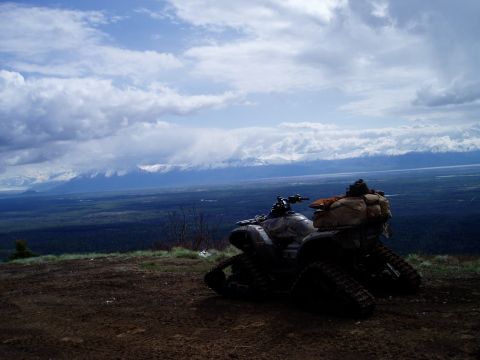 2000 Ford E350 - Two ATVs are parked on a dirt hill with a vast landscape of trees and mountains in the background under a cloudy sky.
