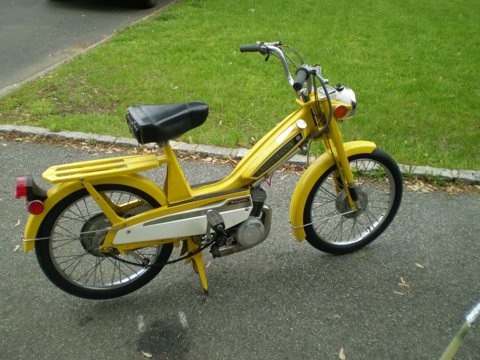 Yellow vintage moped with black seat parked on a paved driveway