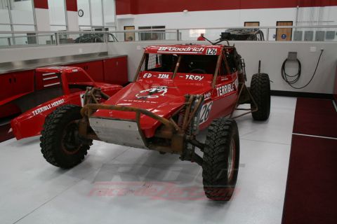 1989 Ford Bronco - A custom-built red buggy with racing decals sits in a garage next to another red vehicle body.