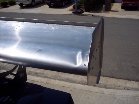 1971 Ford Mustang - A dented aluminum rear spoiler with an OMP logo is attached to a vehicle, with other cars visible in the background.