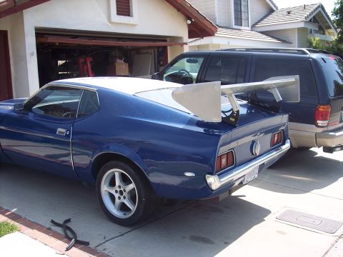 1971 Ford Mustang - A blue coupe with a large rear spoiler is parked in a driveway next to an SUV.