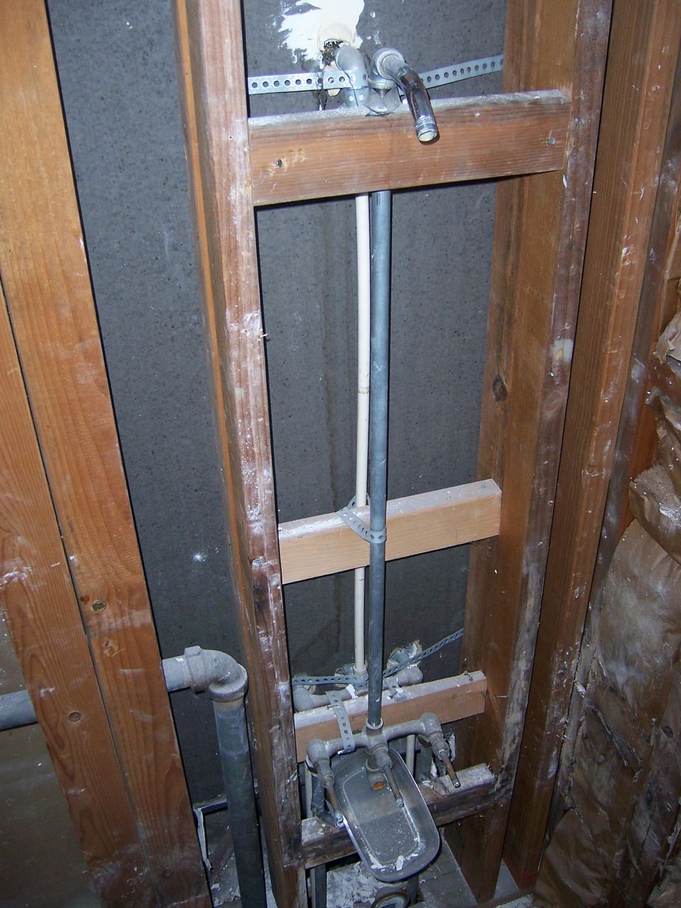 Exposed plumbing pipes and shower valve assembly within wooden framing