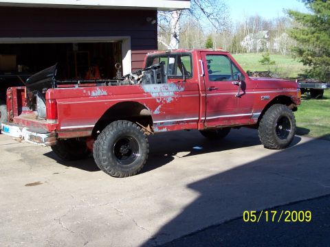 1989 Ford F-150 - This red 1989 Ford F-150 pickup truck features a lifted suspension and oversized tires, suggesting off-road modifications.