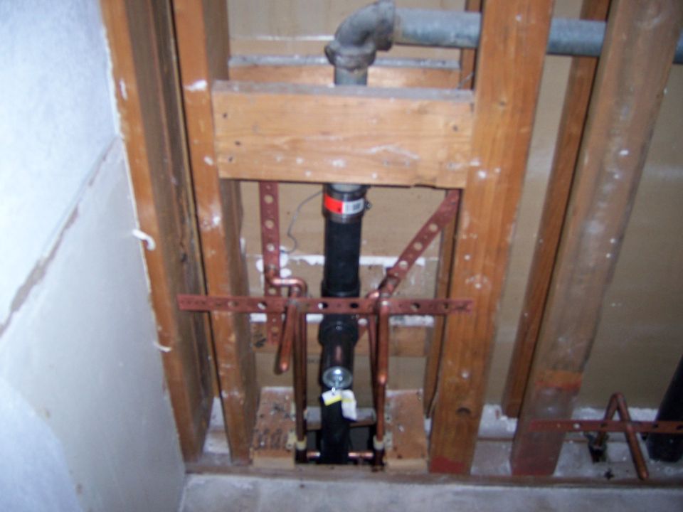 Exposed plumbing pipes and copper fittings within wooden wall studs