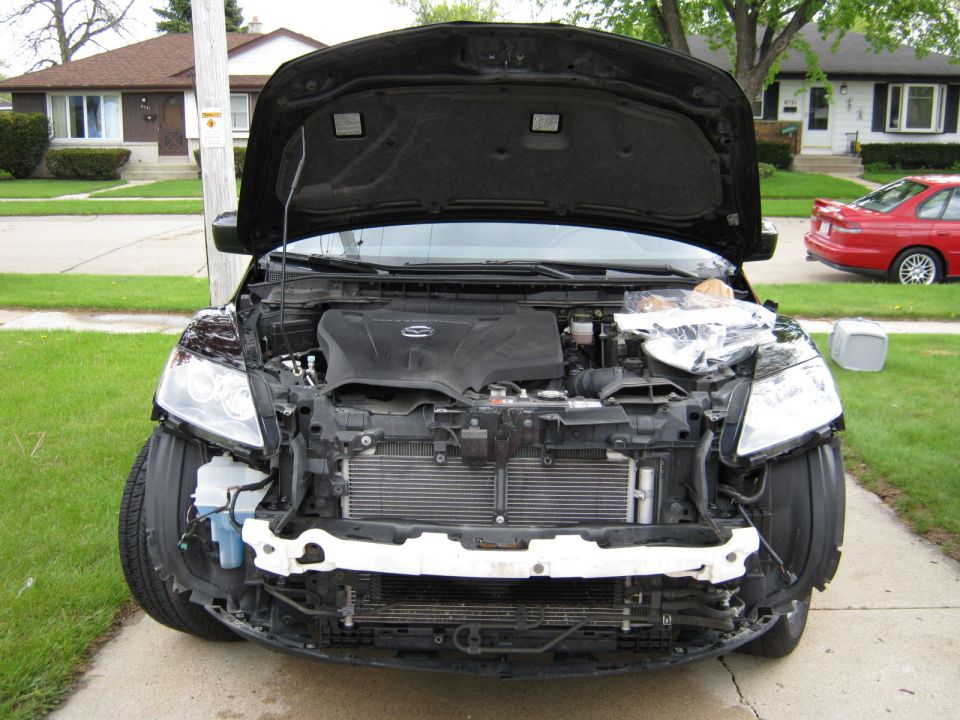 2007 Mazda CX-7 front end with hood open, bumper removed, showing engine and radiator. Red car in background