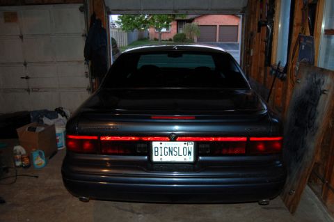 1985 Mercury Grand Marquis - The rear of a dark sedan is parked inside a garage, with a license plate reading BIGNSLOW.
