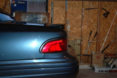 1985 Mercury Grand Marquis - The rear of a blue sedan is visible, with a small black spoiler mounted above the taillight.