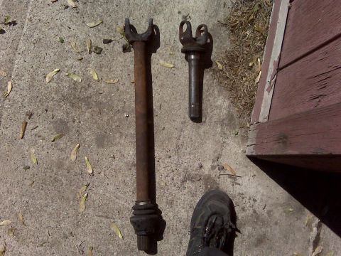 1995 Ford Bronco - Two driveshaft components are shown resting on a concrete surface next to a wooden structure.