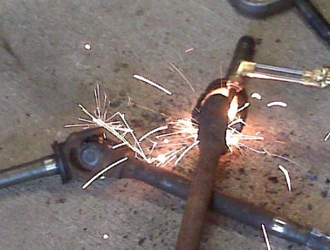 1995 Ford Bronco - A vehicle drive shaft is being cut with a torch, creating a shower of sparks.
