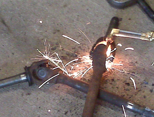 Drive shaft being cut with a torch, sparks flying. Part of a vehicle component