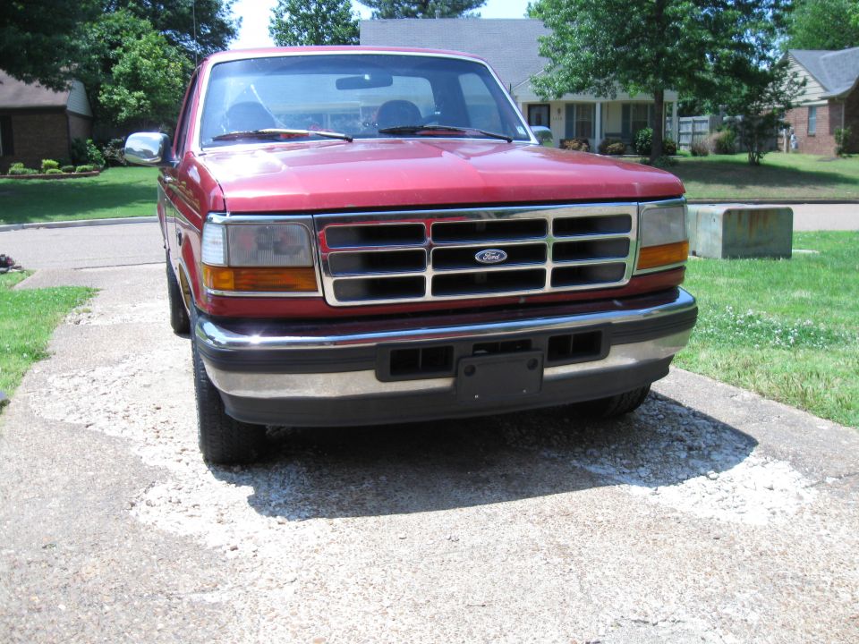 Red 1996 Ford F-150 parked on a gravel driveway, front view