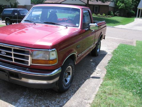 1996 Ford F-150 - A red Ford F-150 pickup truck is parked in a residential driveway next to a lawn.