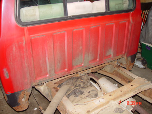 Interior cab corner of a red pickup with the bed removed and floor exposed