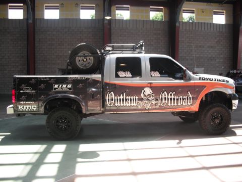 1986 Ford Bronco - This heavily modified pickup truck features custom graphics and off-road modifications, including a roof-mounted spare tire.