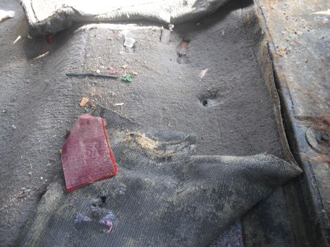 1986 Ford Bronco - The interior floor of a vehicle shows significant wear and tear, with debris scattered across the carpet.