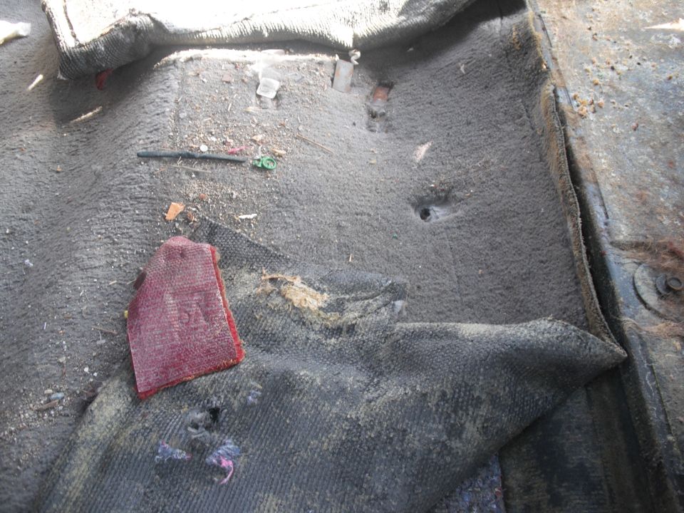 Dirty vehicle floor with torn carpet, debris, and a red fabric swatch