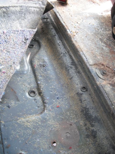 1986 Ford Bronco - Close-up view of the interior floor of a vehicle, revealing the metal structure beneath the carpet and insulation.
