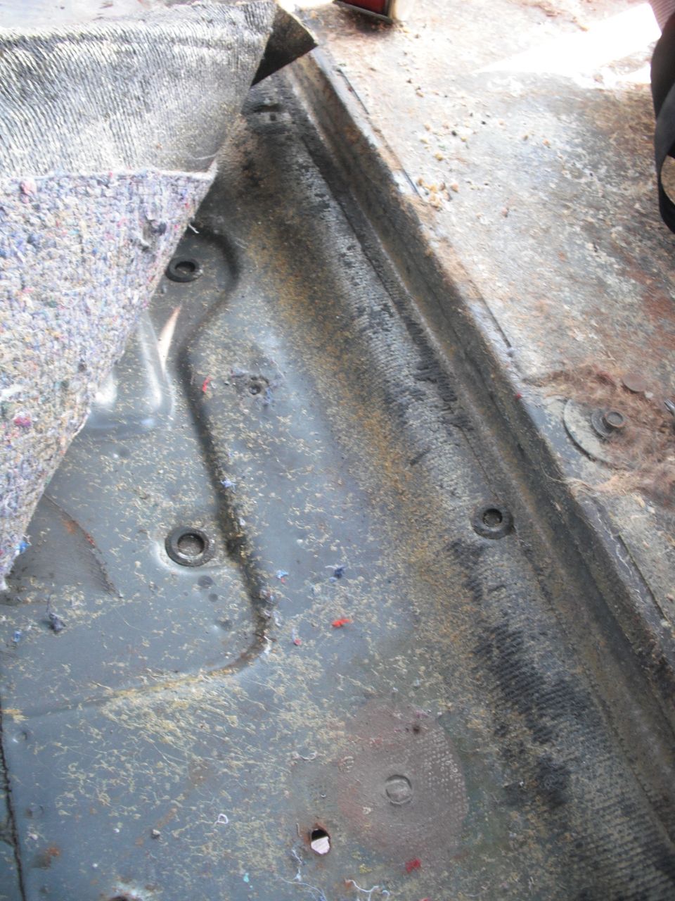 Vehicle floor interior with carpet pulled back, showing metal and mounting points