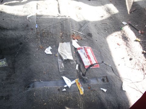 1986 Ford Bronco - The interior floor of a vehicle is littered with trash and debris.
