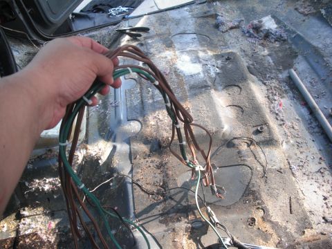 1986 Ford Bronco - The interior floor of a vehicle is exposed, showing dirt, debris, and a bundle of wires.