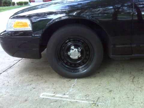 2001 Ford Crown Victoria - Front view of a black 2001 Ford Crown Victoria, showing the fender and a steel wheel with a chrome center cap.