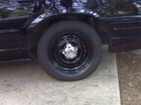 2001 Ford Crown Victoria - Rear wheel and fender detail of a black 2001 Ford Crown Victoria with a steel wheel.