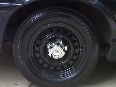 2001 Ford Crown Victoria - Close-up of a black steel wheel with a chrome Ford hubcap on a 2001 Ford Crown Victoria.