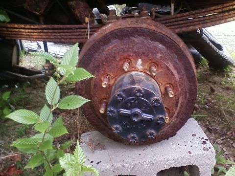 1990 Ford Bronco - Close-up of a heavily rusted wheel hub and brake drum, with green foliage in the foreground.