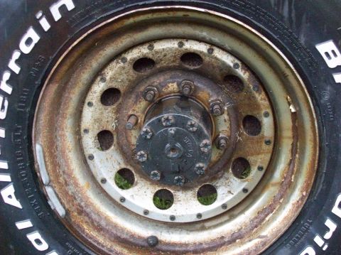1985 Ford F-250 - A close-up view of a rusty wheel hub and tire, showing the details of the lug nuts and the tire's sidewall markings.