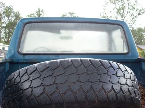 1985 Ford F-250 - A spare tire is positioned in the bed of a blue pickup truck, obscuring the rear window.