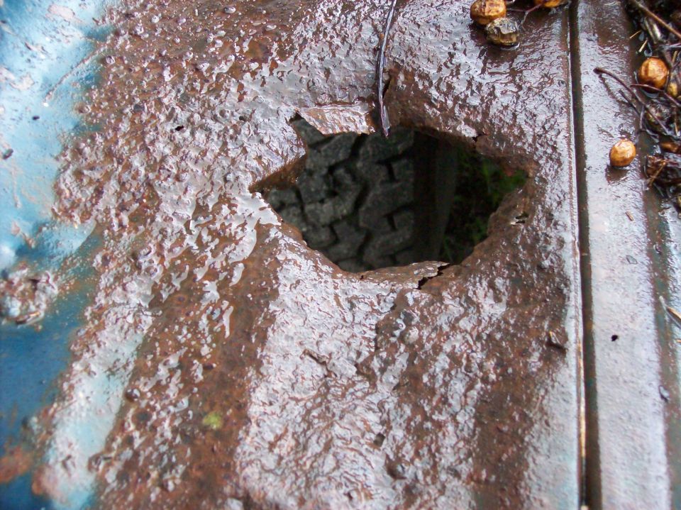 Rusted blue metal bed with a large hole revealing a tire tread below
