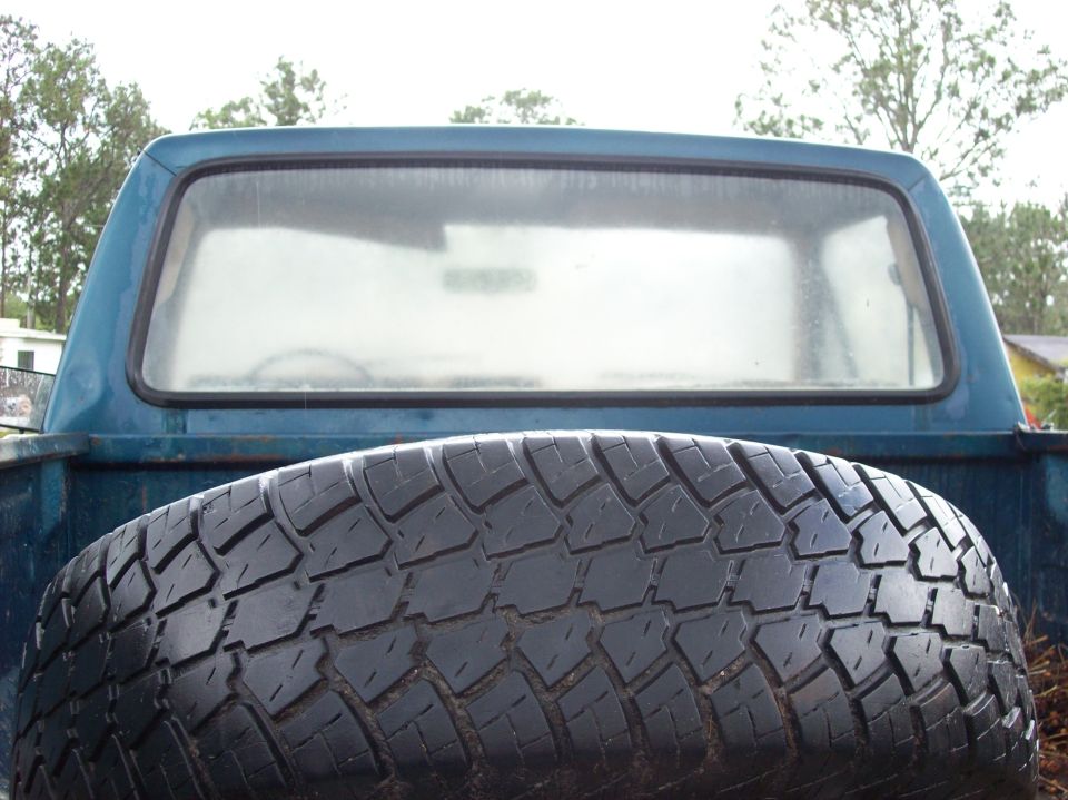 Spare tire in the bed of a blue pickup truck, showing the rear window