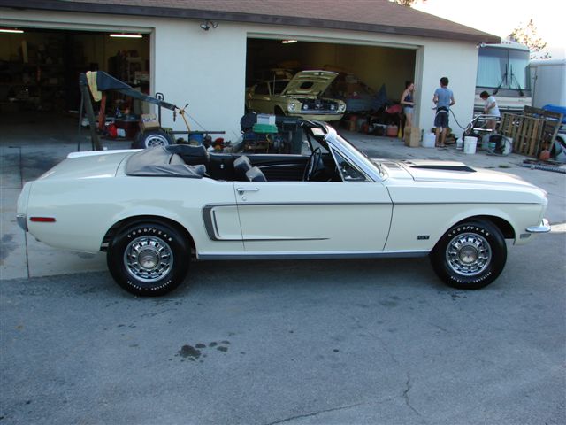 White classic Ford Mustang convertible parked outside a garage