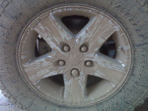 2008 Jeep Wrangler - A close-up of a muddy Jeep Wrangler wheel and tire, showing the tread pattern and five-spoke design.