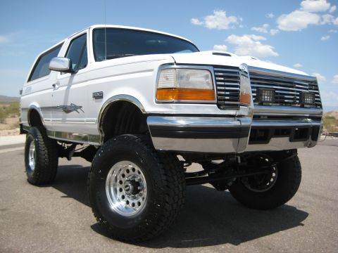 1996 Ford Bronco - This lifted SUV has a prominent chrome grille and is parked behind another vehicle.