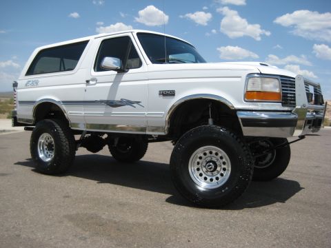 1996 Ford Bronco - This white Ford Bronco SUV features a lifted suspension and off-road tires, viewed from the front three-quarter angle.