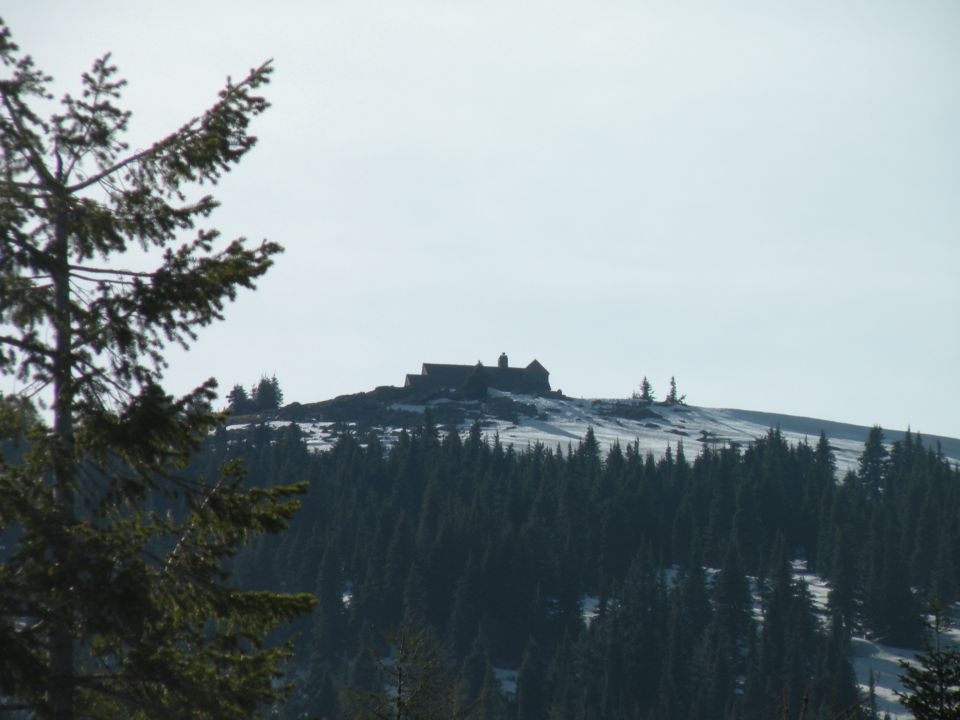 Building on a rocky, snow-dusted hilltop above a dense forest of dark green pine trees