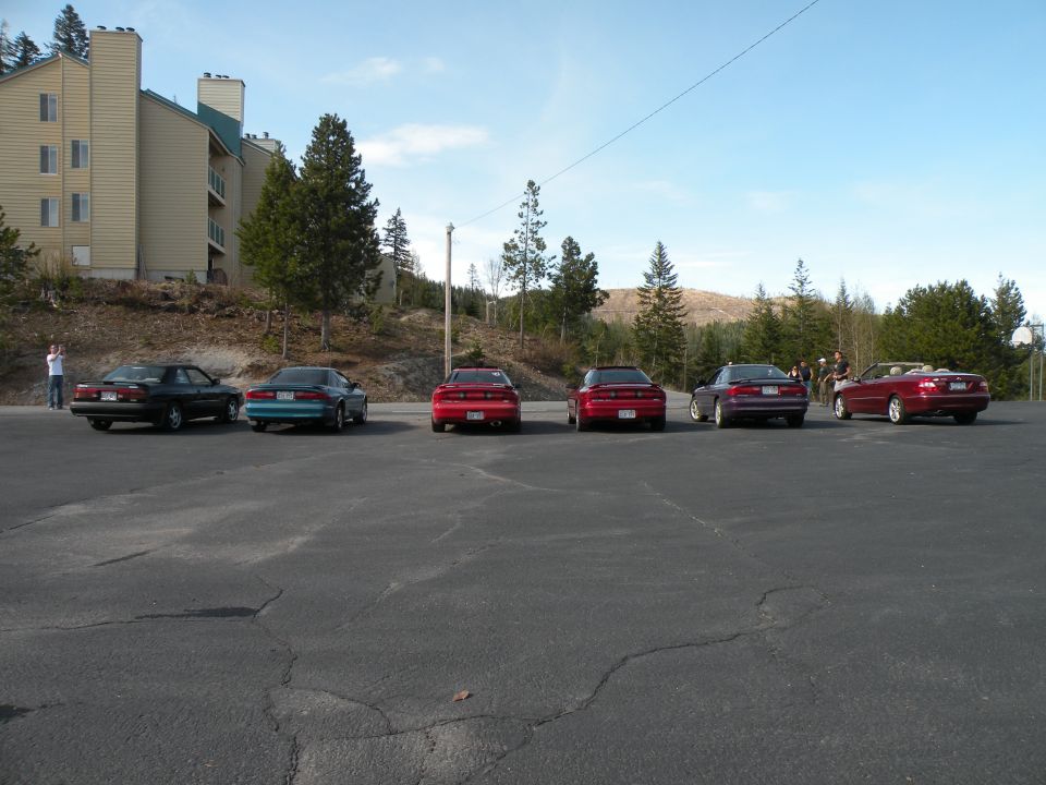 Six Nissan 300ZX cars parked in a lot, viewed from the rear. One is red, one is teal, two are red, one is dark purple, and one is red convertible