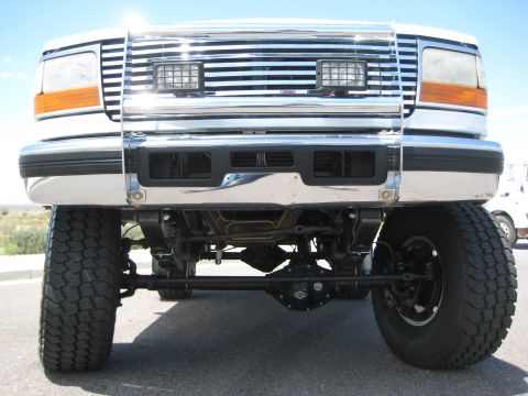 1996 Ford Bronco - This lifted truck features a prominent chrome grille and large tires, with visible suspension components underneath.