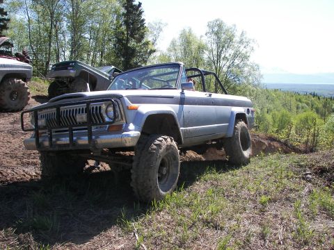 1990 Chevrolet Suburban - This modified SUV navigates a challenging off-road course with other vehicles visible in the background.