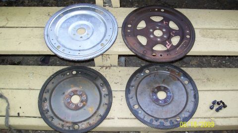 1973 Mercury Cougar - A collection of four flexplates, showing varying degrees of wear and rust, are displayed on a wooden surface.