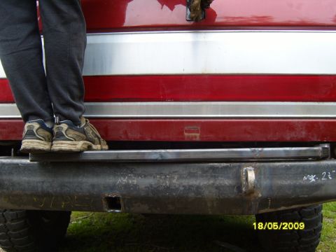 1989 Ford Bronco - Aftermarket rear bumper with tow hitch receiver and step, above red and silver body panels.