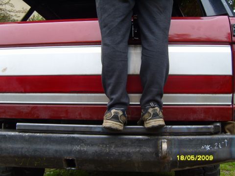 1989 Ford Bronco - A person stands on the rear bumper of a red vehicle with distinctive side trim.