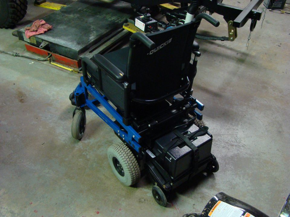 Power wheelchair with blue frame and black seat, sitting on concrete floor