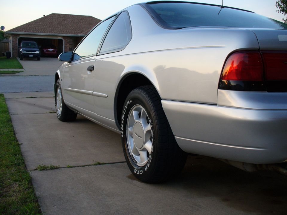 Silver 1995 Ford Thunderbird parked in driveway, rear quarter view. Two other vehicles visible in garage