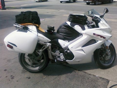 1985 Ford LTD Crown Victoria - A white Honda VFR motorcycle equipped for touring is parked on a street.