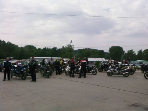 1985 Ford LTD Crown Victoria - A group of motorcyclists and their bikes are assembled in an outdoor lot under a cloudy sky.
