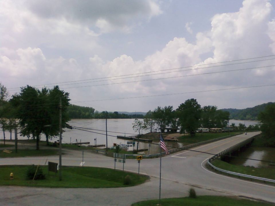 River scene with a bridge, RVs parked near the water, and an American flag